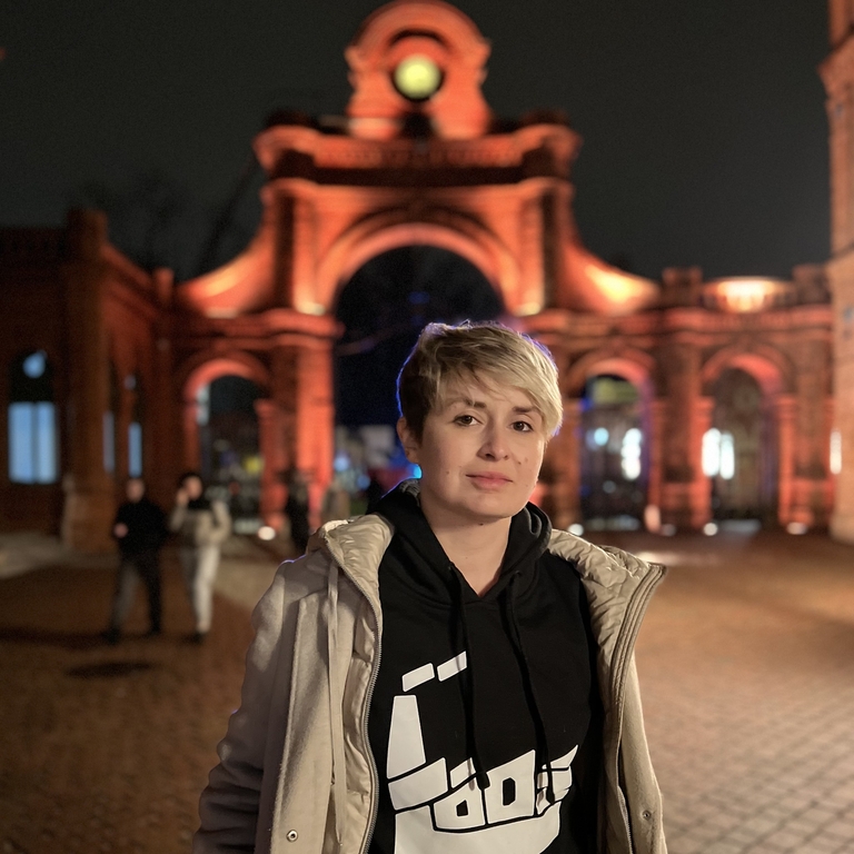 Karolina Głowacka, founder of Radio Naukowe against the background of the entrance gate to the Manufaktura shopping centre illuminated at night